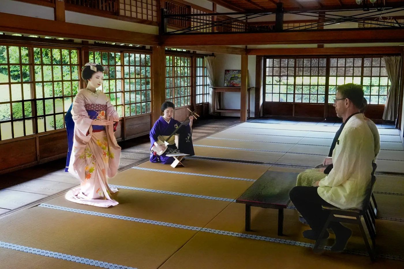 A maiko dancing in a tatami hall while a guest watches from a chair