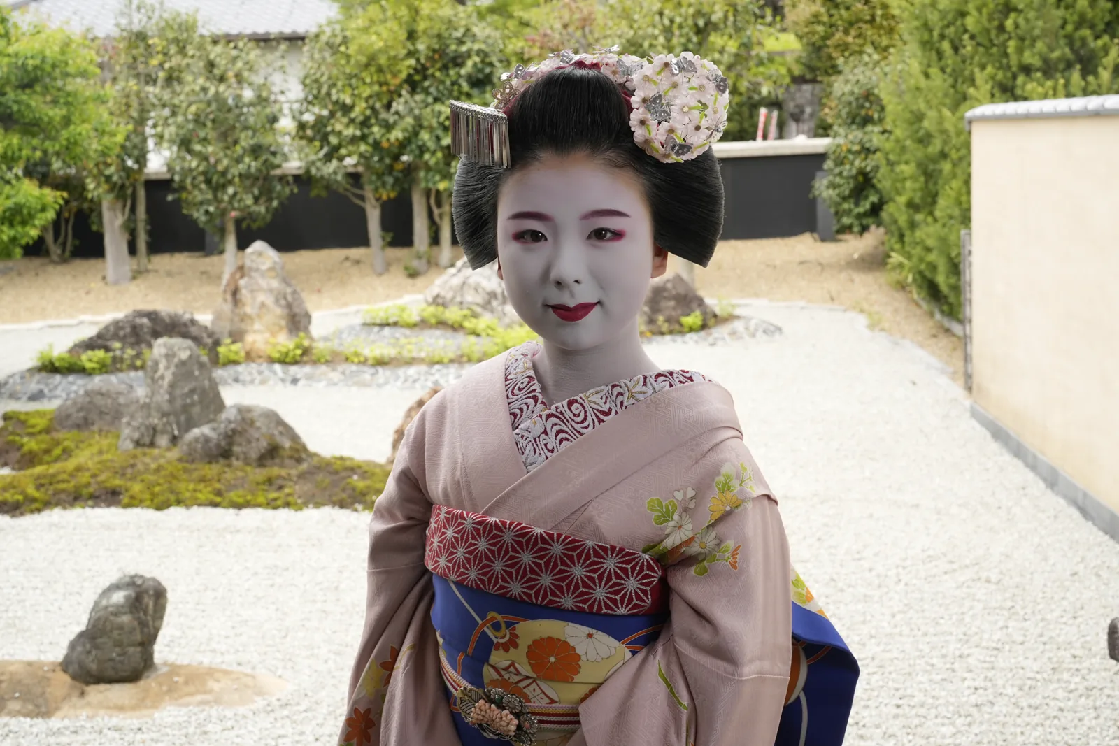 Maiko with kanzashi hair ornaments and white makeup in a temple rock garden