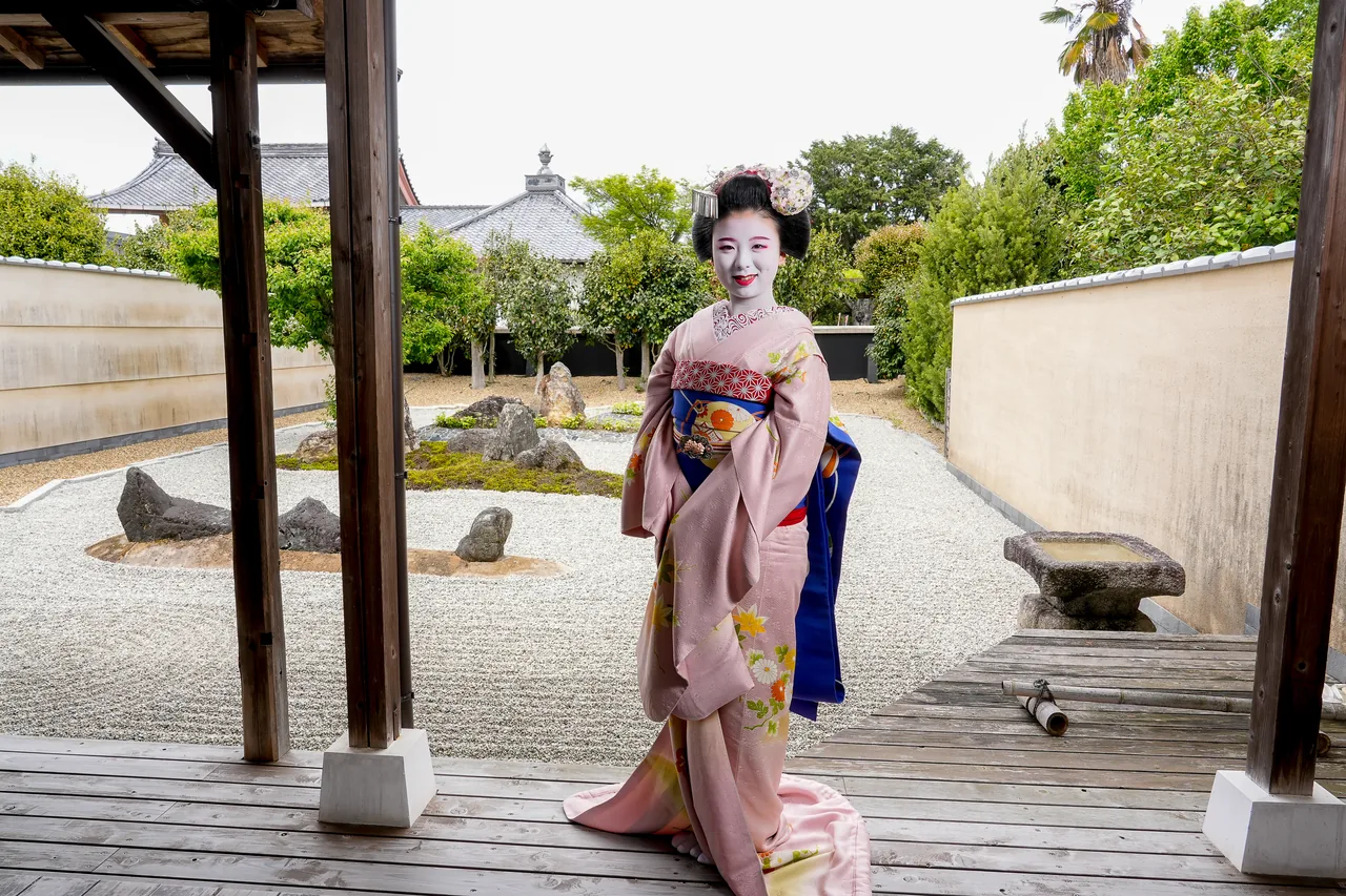 Maiko in full dress with kanzashi and a long obi in front of a temple rock garden