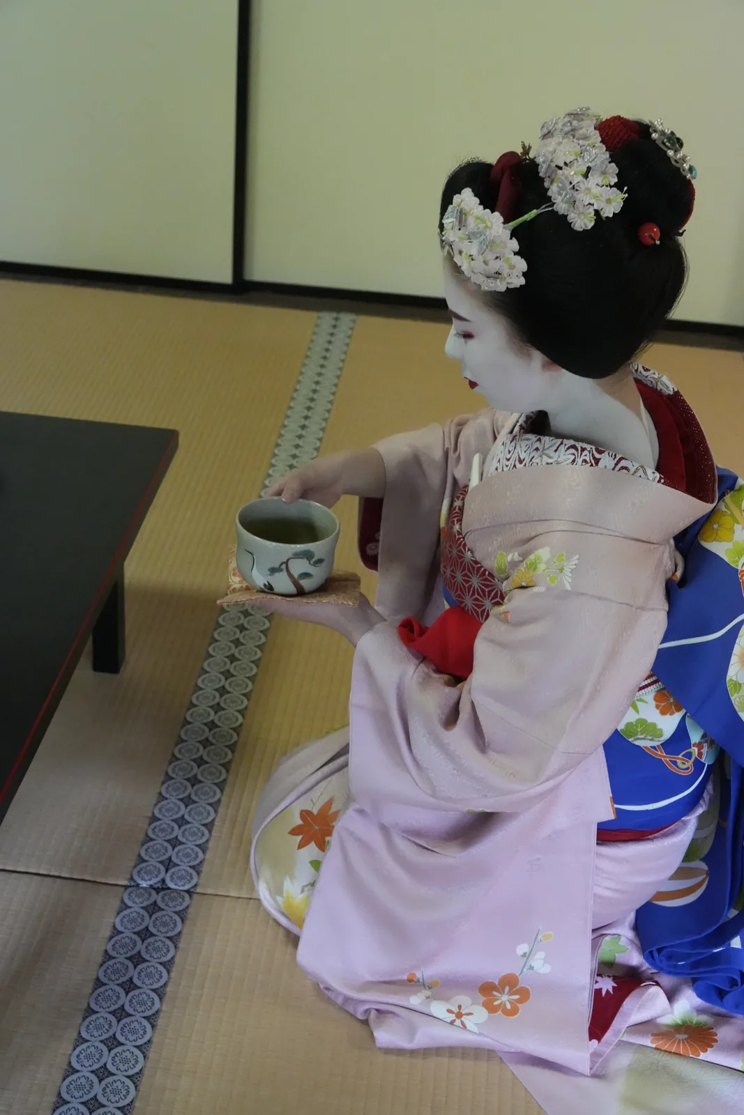 Maiko offering a cup of tea on tatami in a temple hall