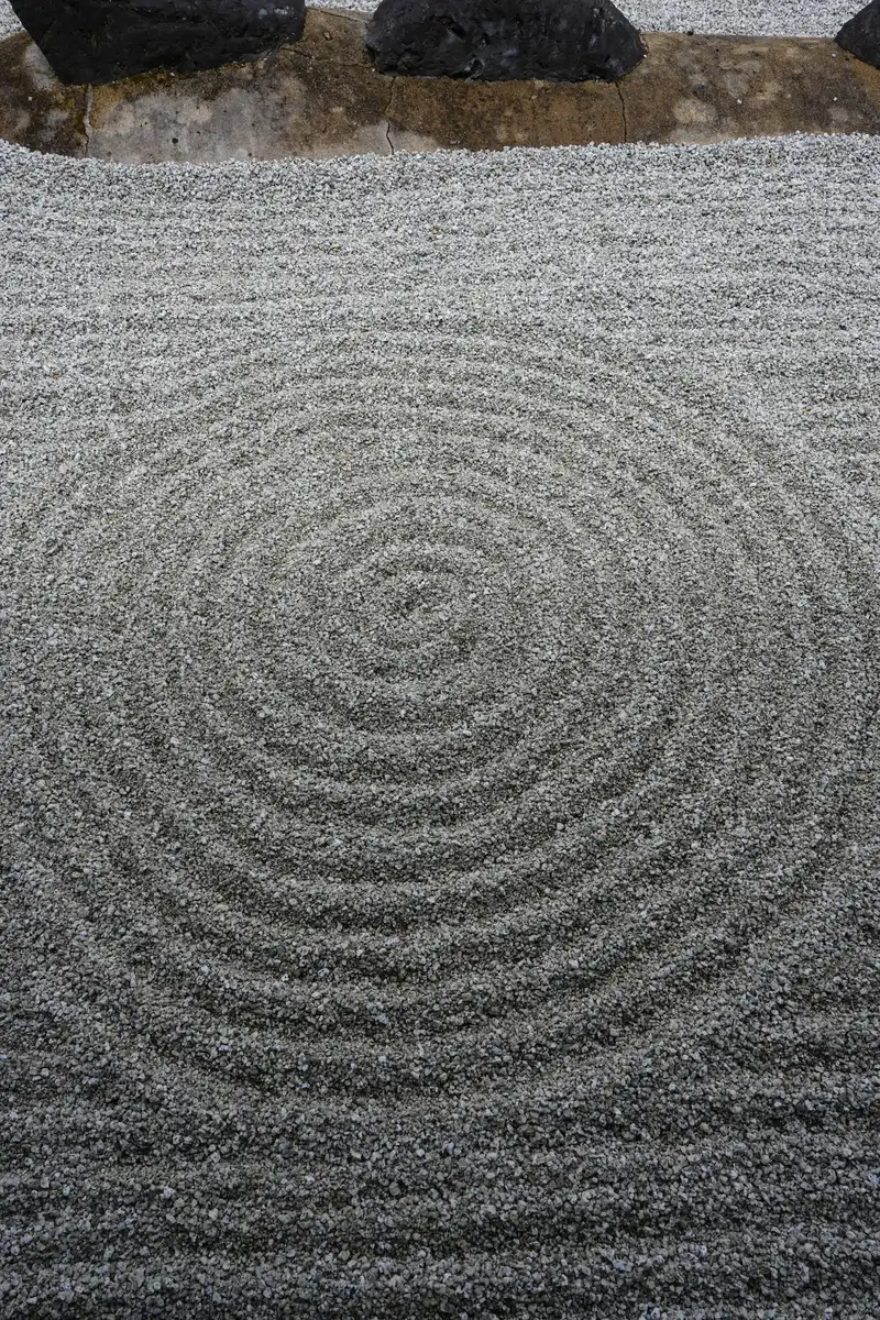 Concentric rings and straight lines raked into gray gravel below a row of dark stones