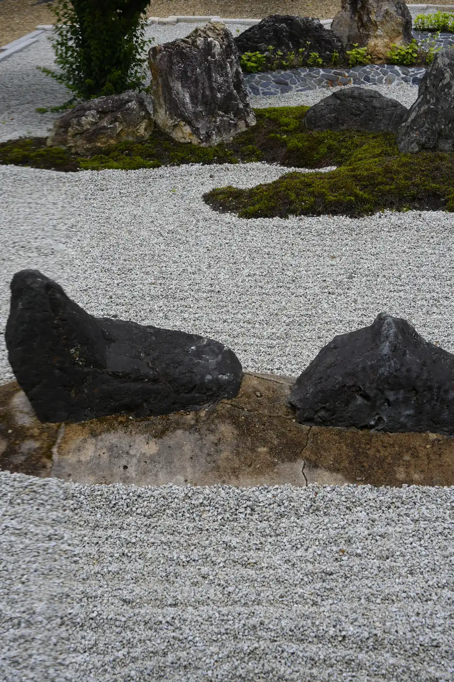 Dark stones on a flat base in front, with taller stones and moss behind, in white gravel