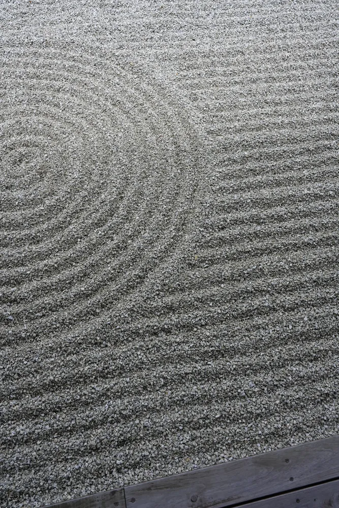 Concentric rings beside straight lines raked into gray gravel, with a wooden edge at the bottom