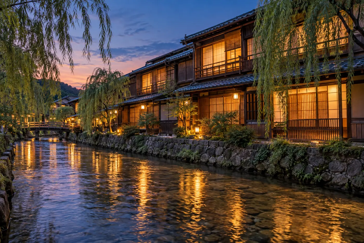 Two-storey wooden teahouses with lit lattice windows along a willow-lined stream at dusk