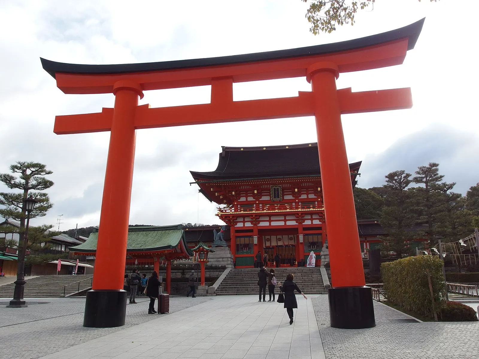 The large vermilion torii and two-storey gate at the entrance of Fushimi Inari Taisha, with visitors in coats