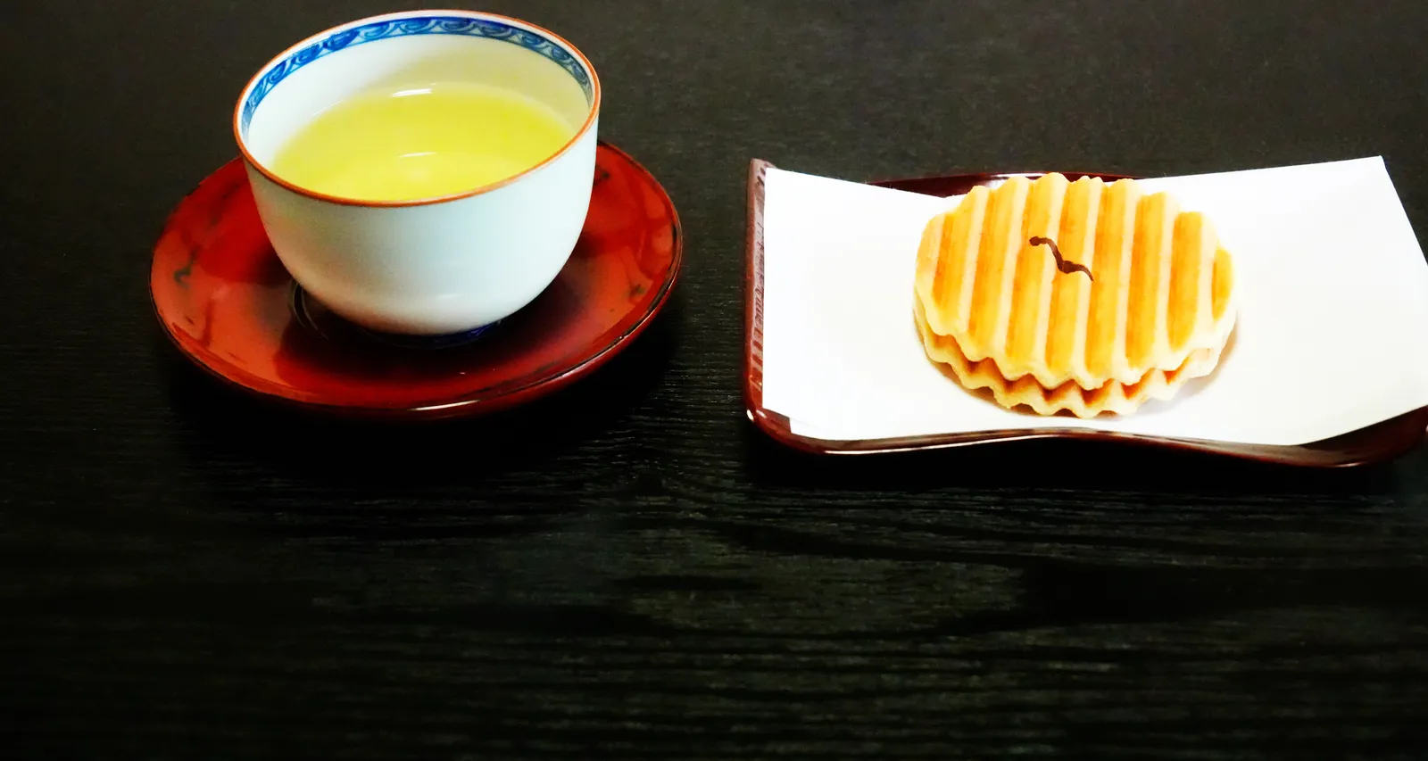 A cup of sencha green tea and a Japanese sweet on a dark table