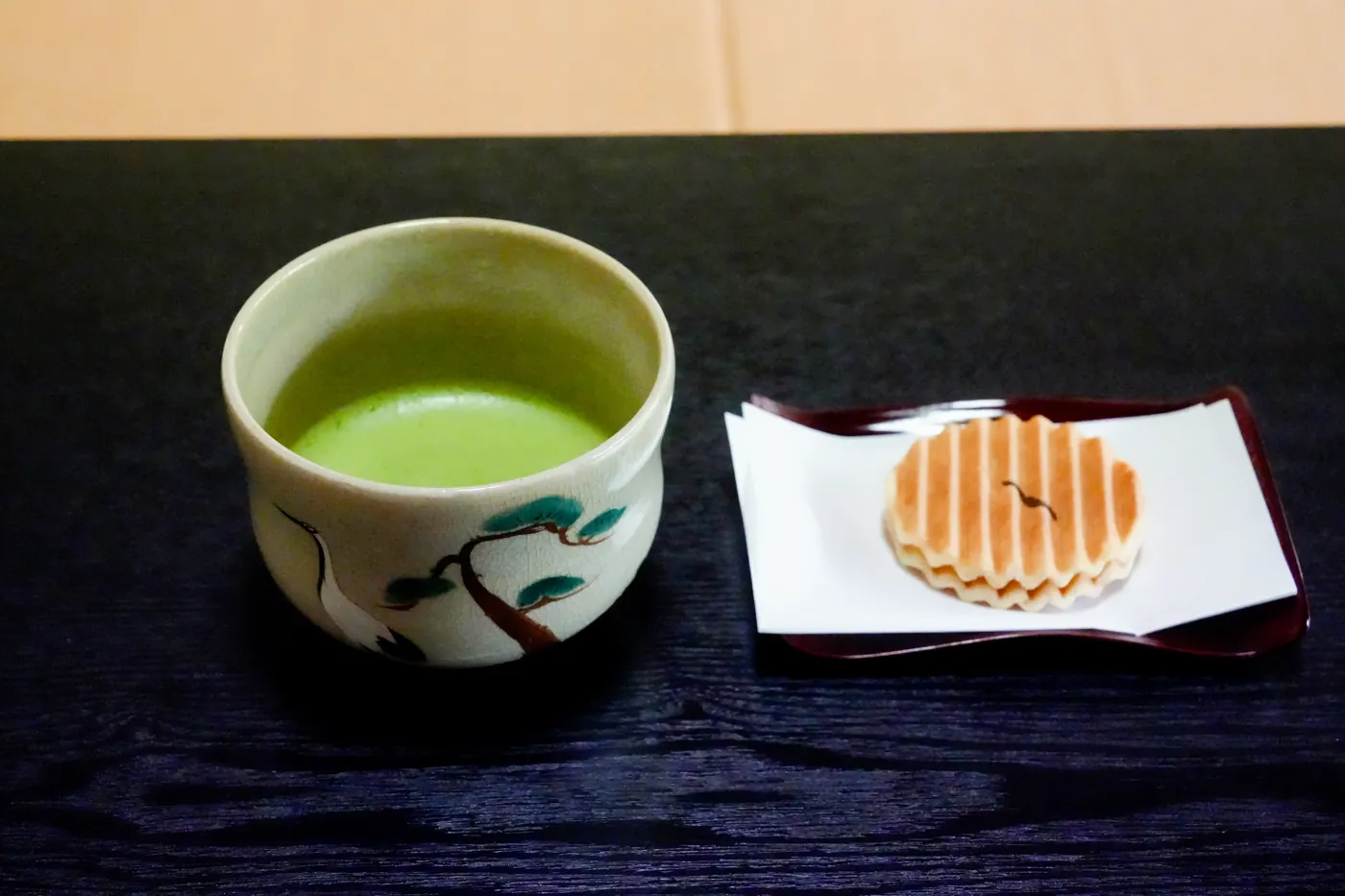A bowl of matcha beside a Japanese sweet on a white plate
