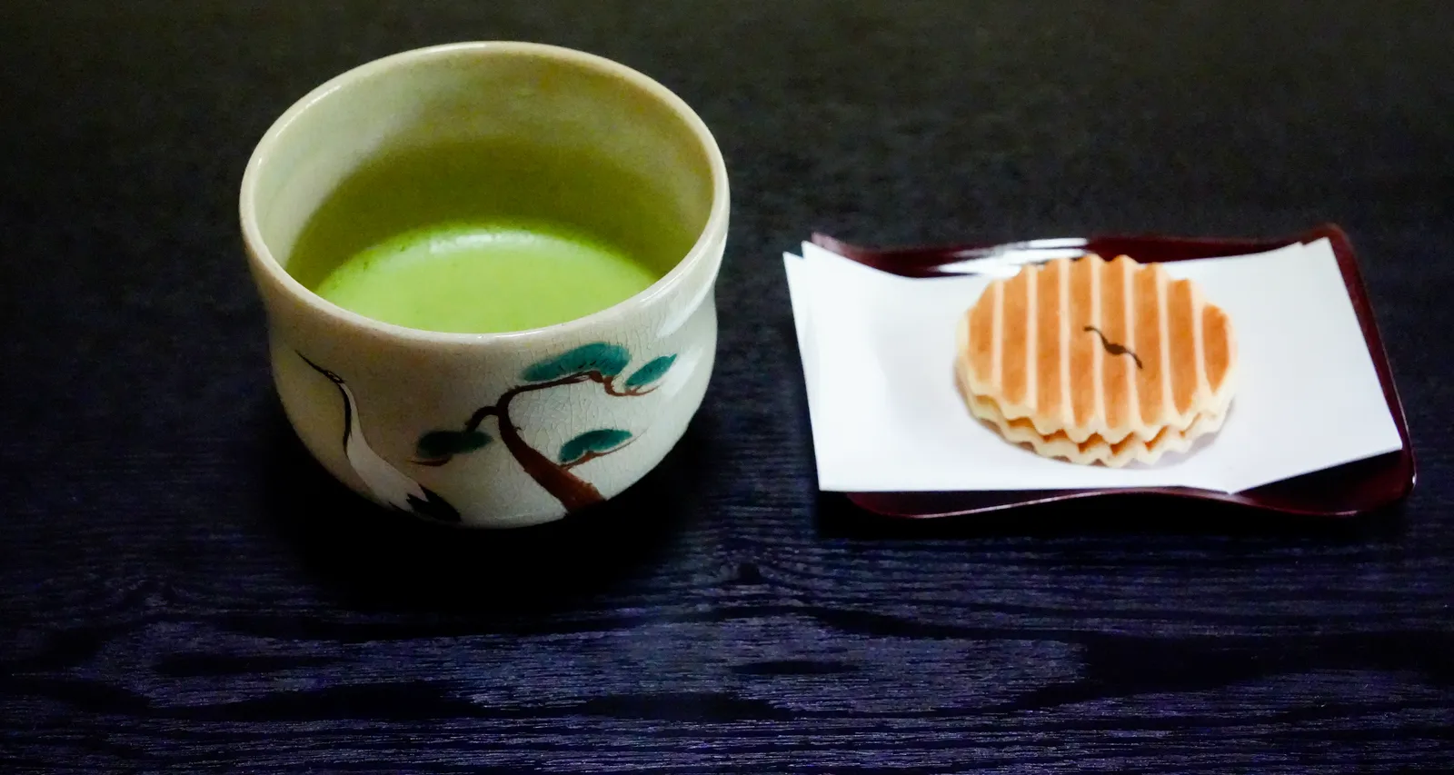 A bowl of matcha and a Japanese sweet on a dark table