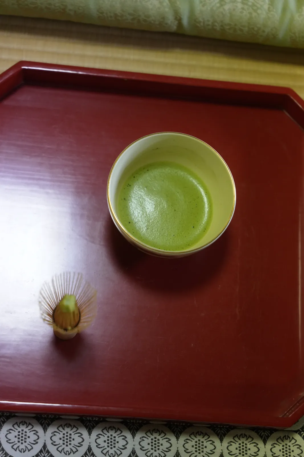 A bowl of whisked matcha and a bamboo whisk on a red lacquer tray