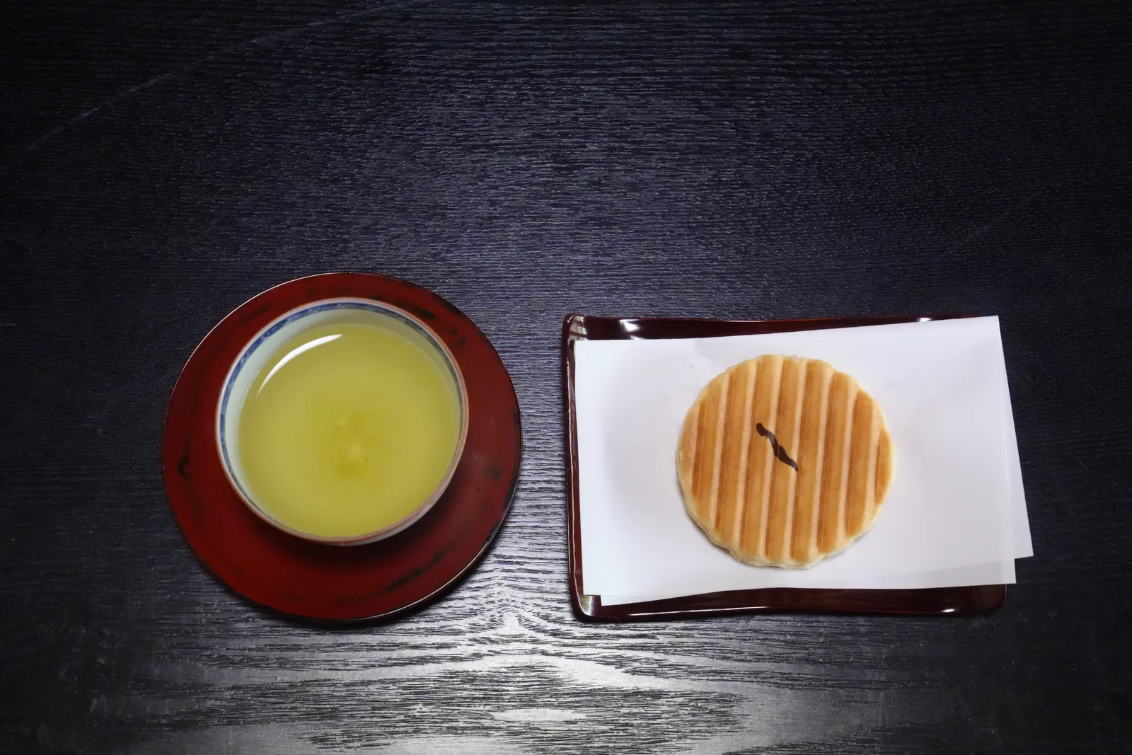 A cup of sencha and a Japanese sweet on a dark table, seen from above