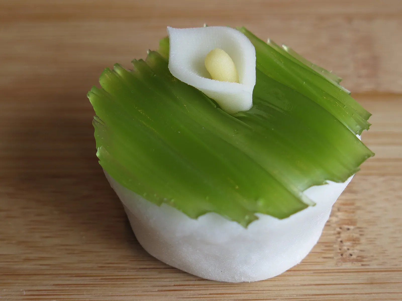 A green wagashi sweet with a glossy top and a small white flower shape