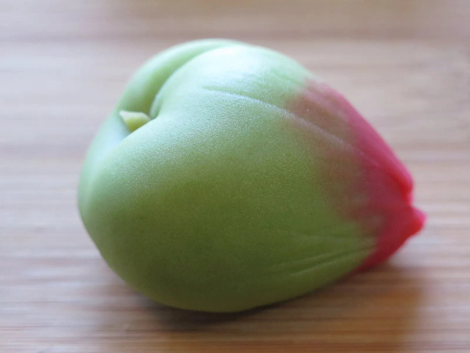A smooth green wagashi sweet with a red-pink tip, shaped like a bud