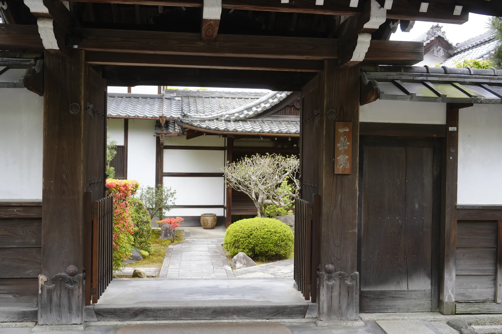 The wooden gate of a Zen temple in Kyoto, with a stone path leading past a pruned shrub to the temple buildings